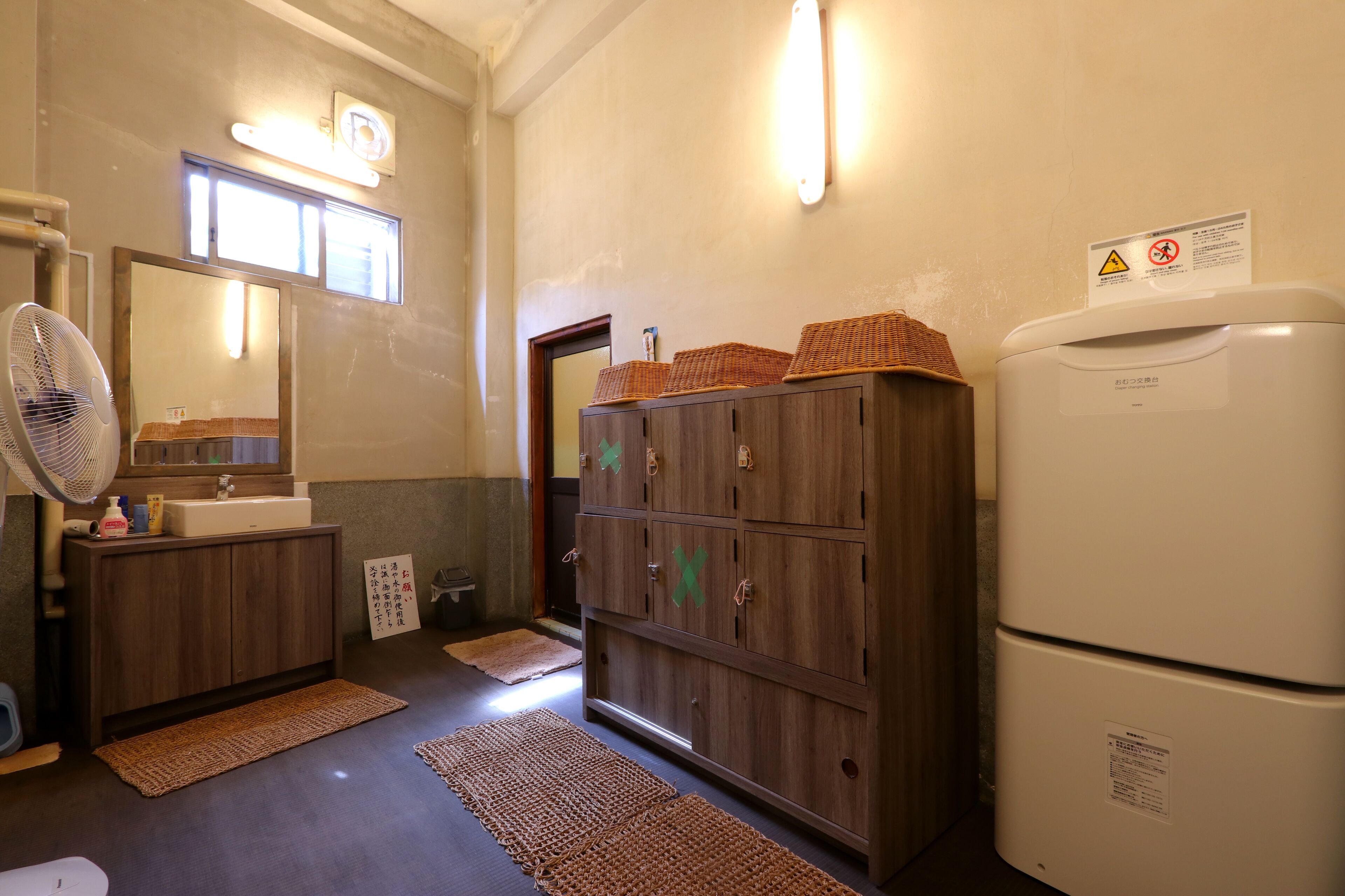 A bathroom with a wooden cabinet, a white sink, a mirror, and a white refrigerator.