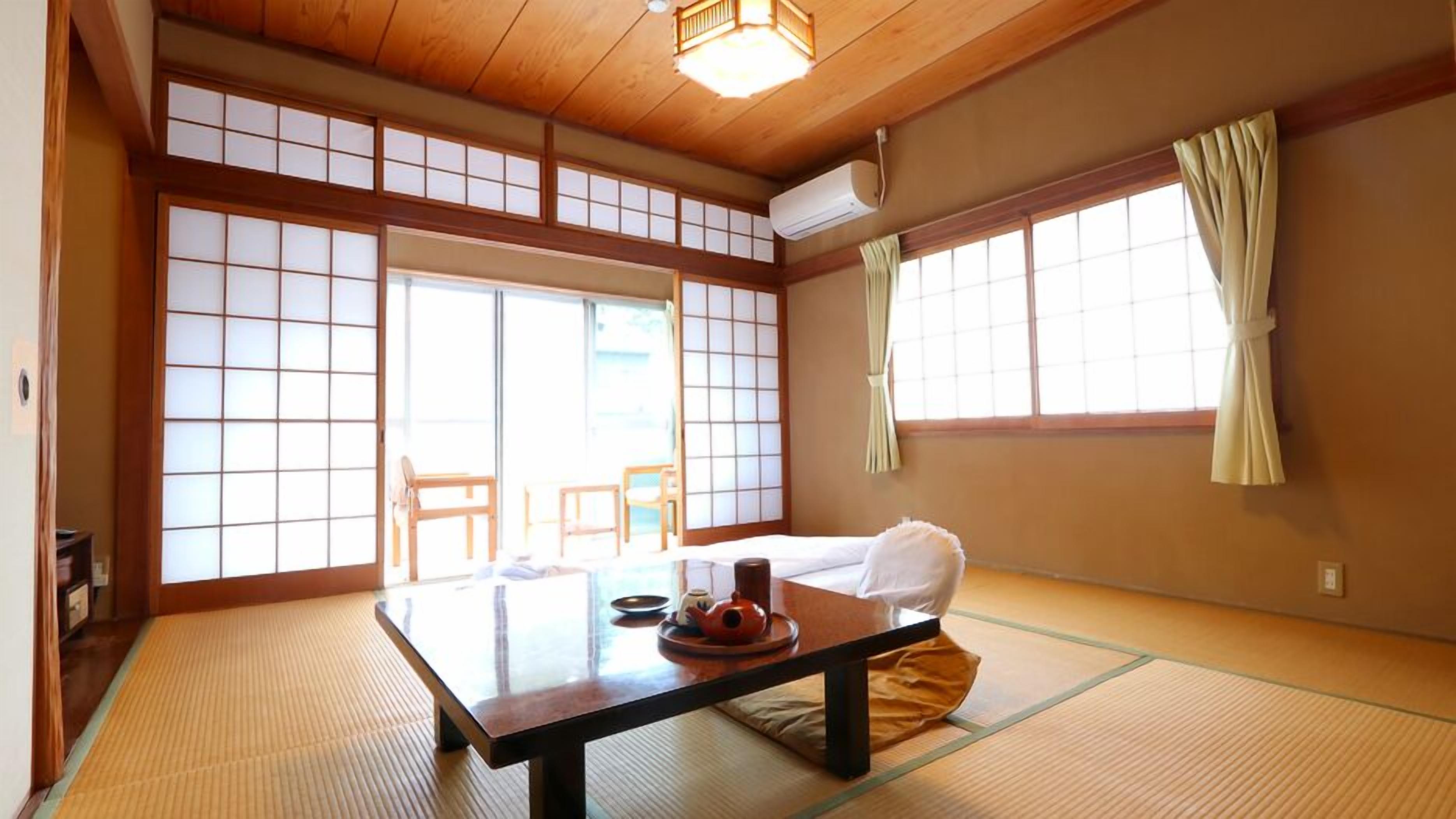 A traditional Japanese room with tatami flooring, a low table with a tea set, sliding doors, and a large window with curtains.