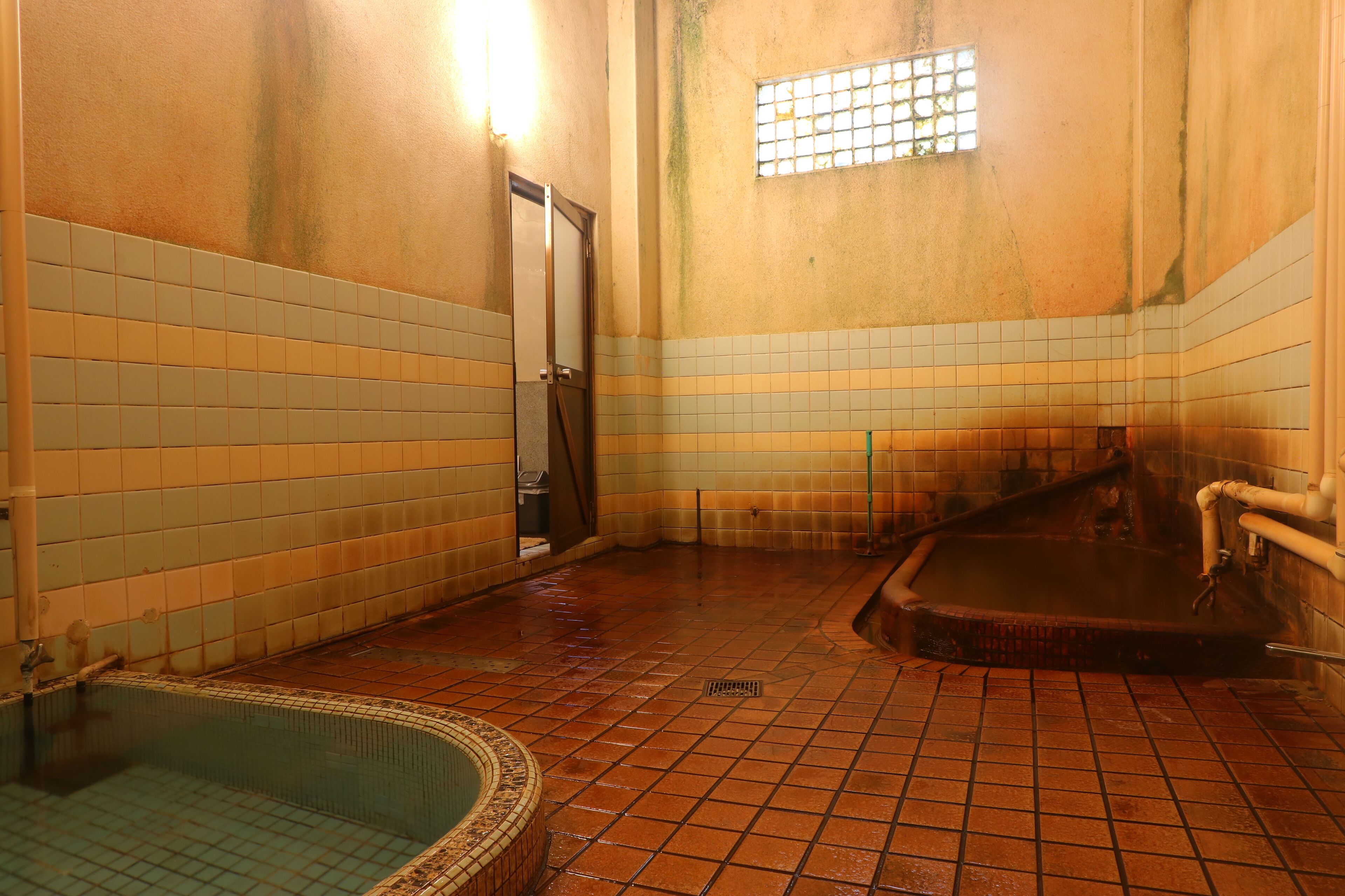 Un espace de bains public doté de murs carrelés, d’une baignoire et d’une petite piscine.
