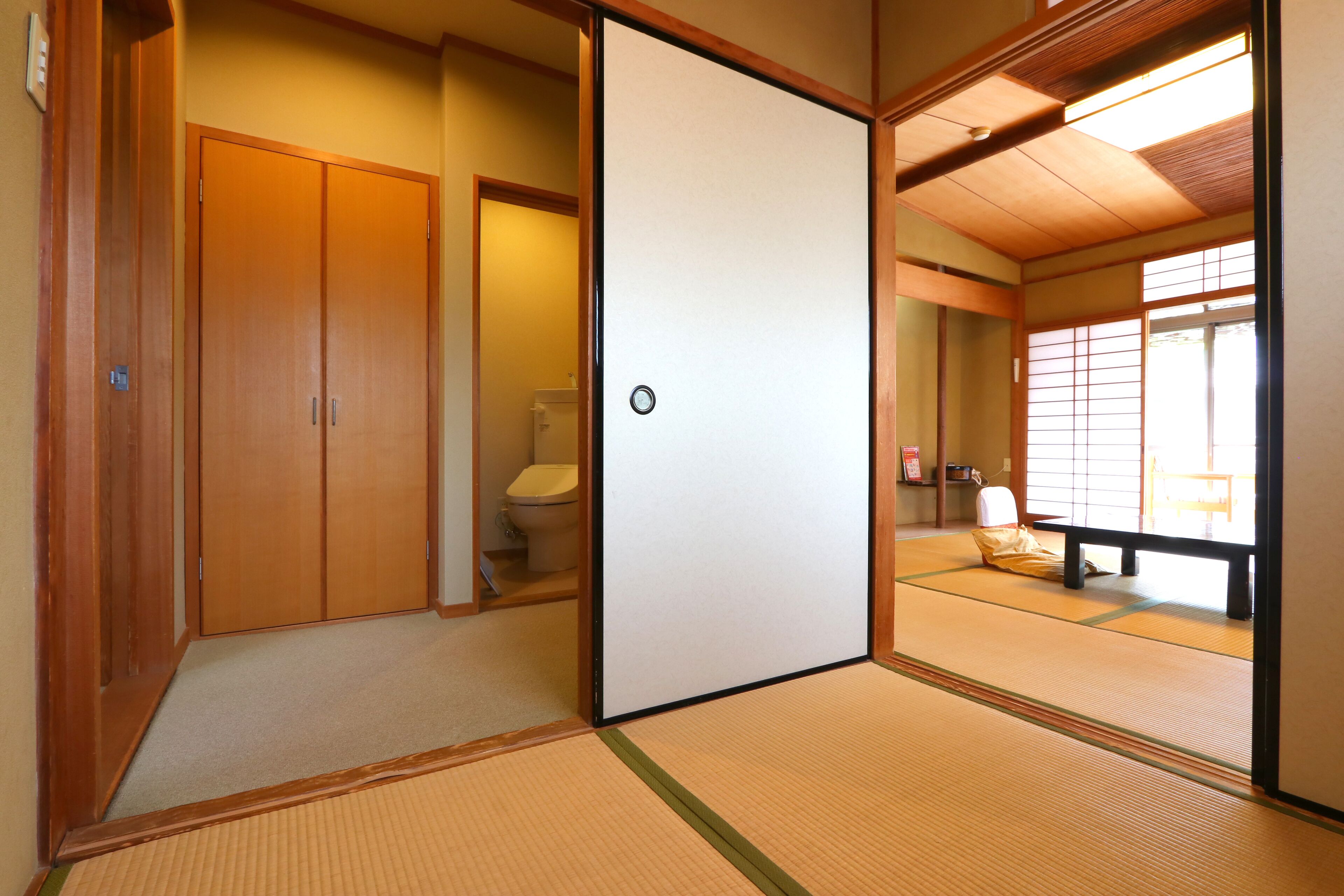 Une pièce de style japonais traditionnel, avec un sol recouvert de tatamis, des portes coulissantes et des toilettes visibles à travers l’une des portes.
