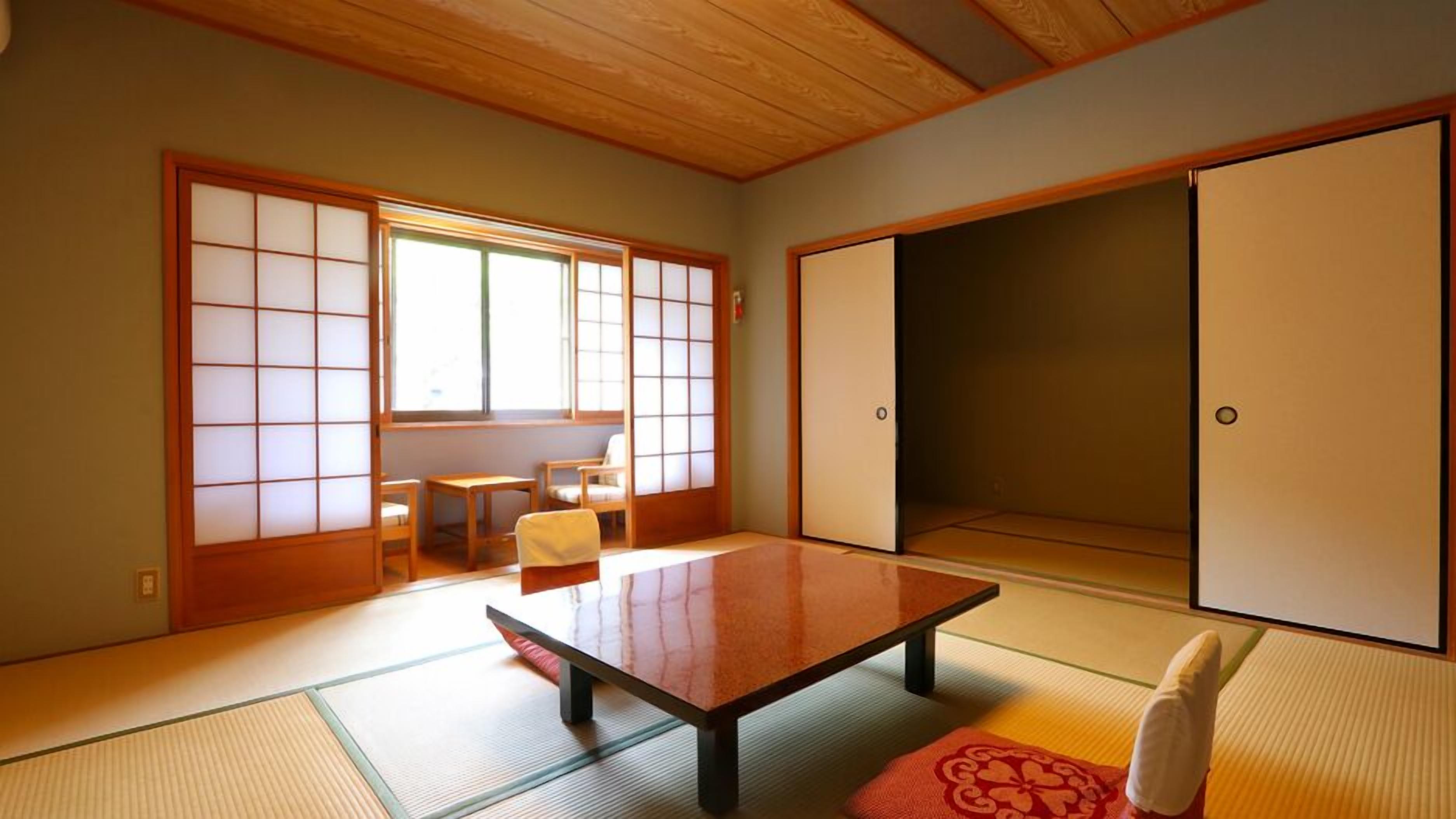 A traditional Japanese room with tatami flooring, a low table, sliding doors, and a view of a garden.