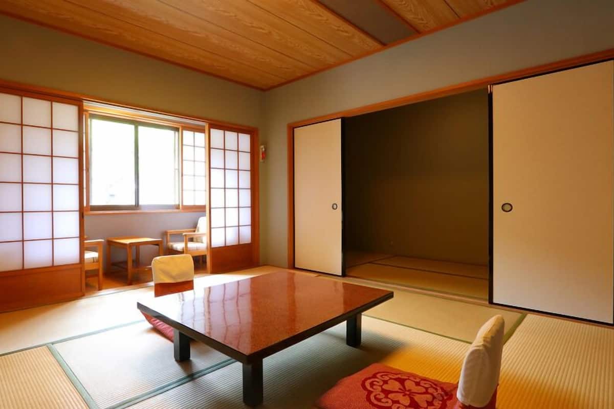 A traditional Japanese room with tatami flooring, a low table, sliding doors, and a view of a garden.