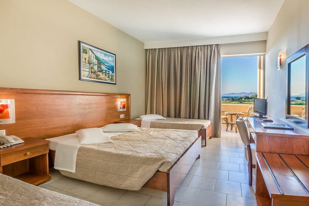 Une chambre d’hôtel avec deux lits, un bureau avec une télévision, un tableau au mur et une vue sur la mer.