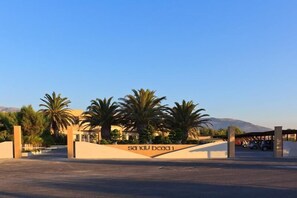 A gated entrance with palm trees and a mountain in the background.