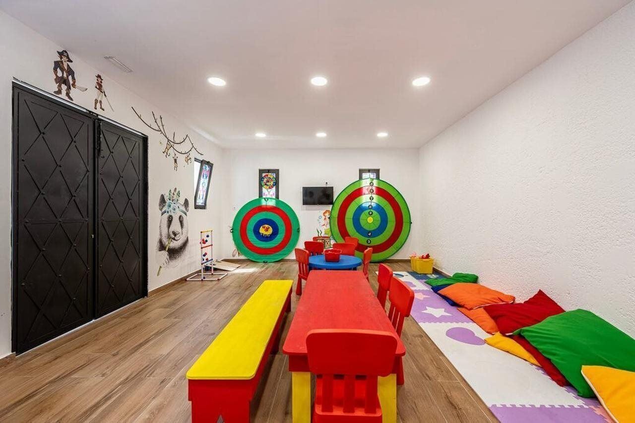 A room with a long table, chairs, a bench, and colorful cushions on the floor.