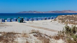 Ein Strand mit Zelten und einem kleinen Gebäude, vermutlich einer Toilette, mit freiem Blick auf das Meer und ferne Hügel.