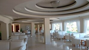 Eine großzügige Lobby mit hoher Decke, modernen Kronleuchtern und verschiedenen Sitzbereichen, darunter Sofas und Sessel.