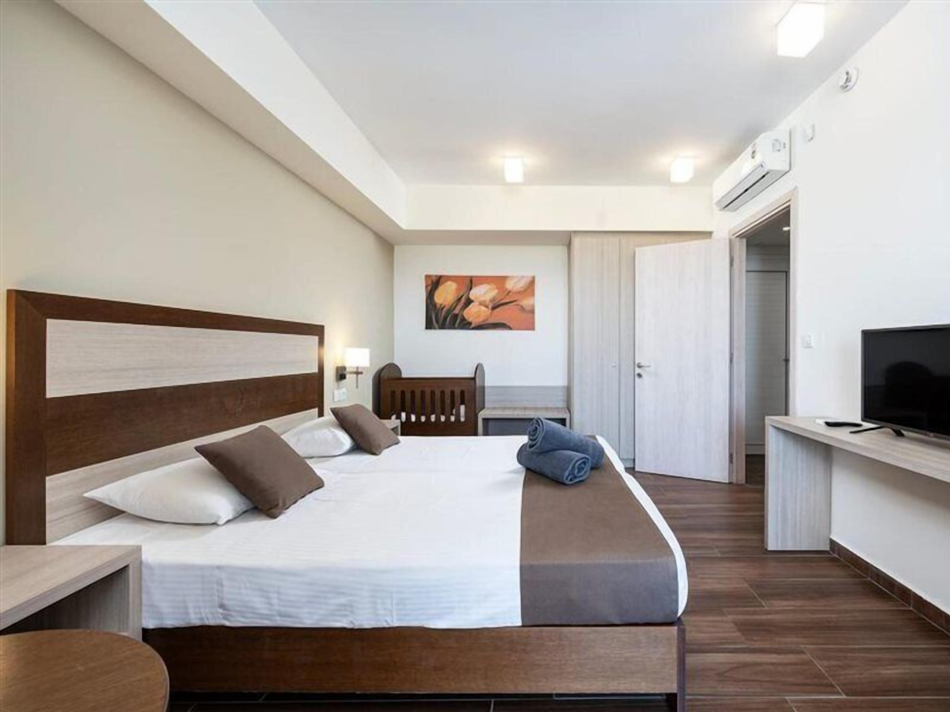 A hotel room with a large bed, a desk, a television, and a painting on the wall.