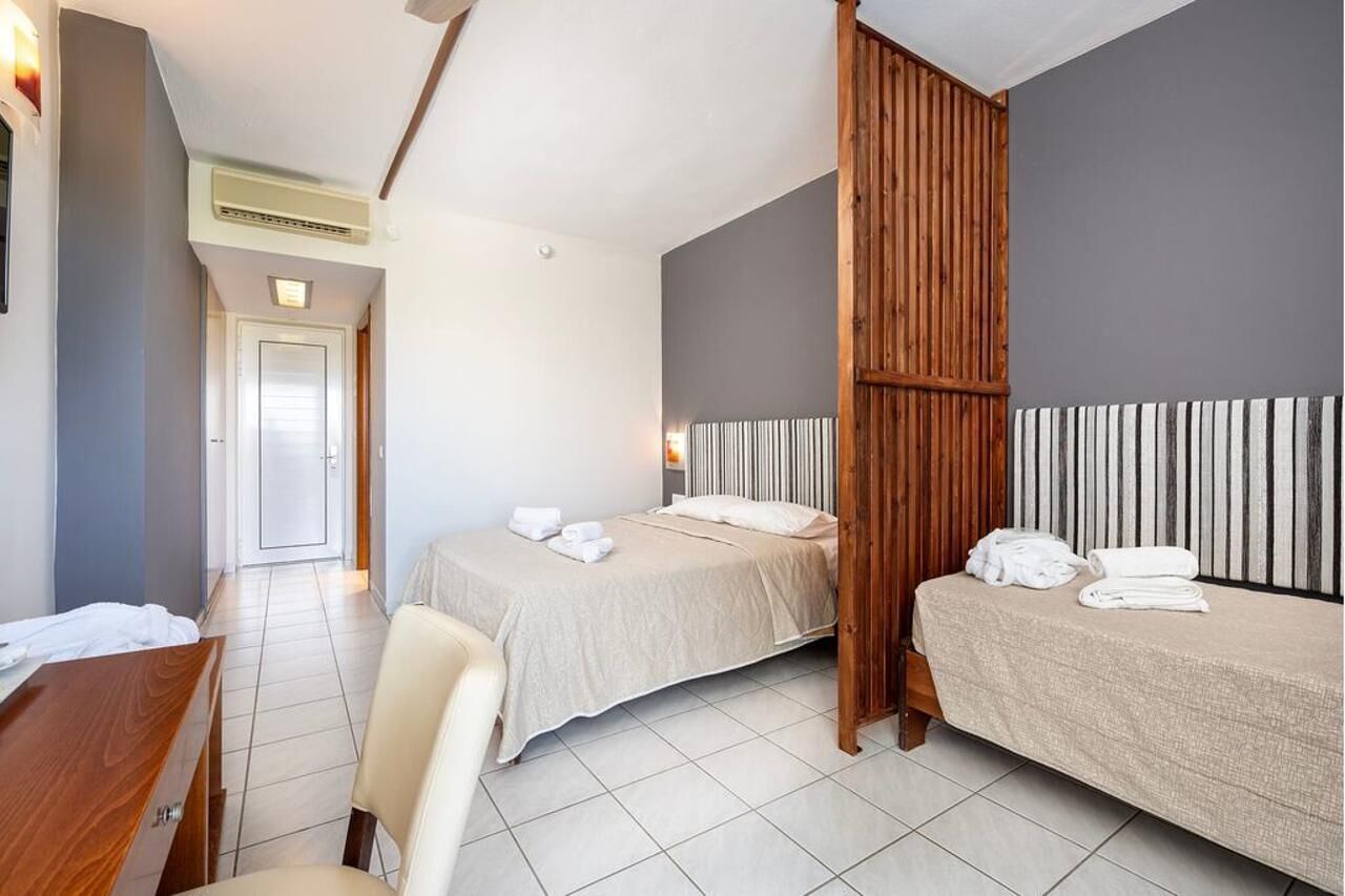 A hotel room with two beds, a desk, a chair, and a wooden partition.