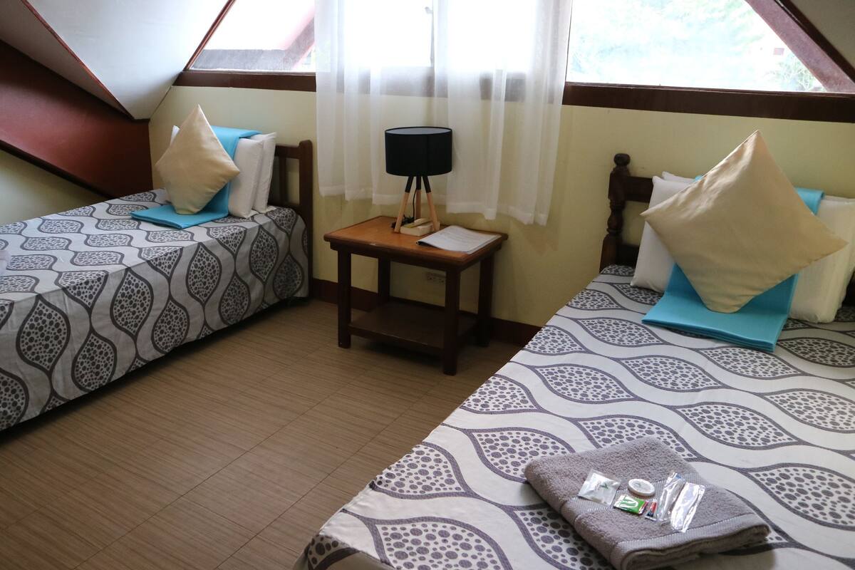 Une chambre avec deux lits, une petite table avec une lampe et une fenêtre avec des rideaux.