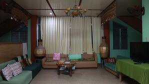 Un salon avec un canapé, une table basse, un téléviseur posé sur un meuble et une table recouverte d’une nappe verte.