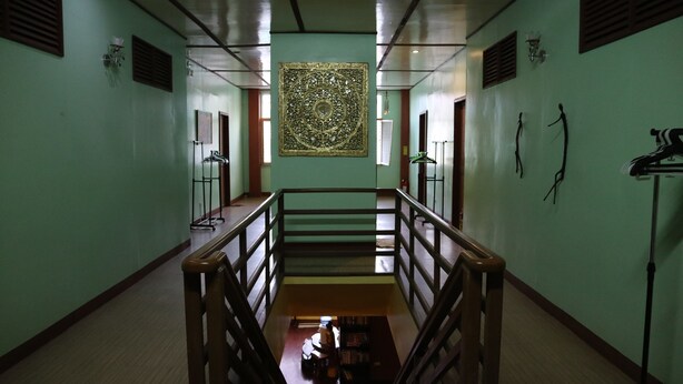 Un couloir avec une rambarde en bois, un grand élément décoratif mural et un escalier menant à un niveau inférieur.