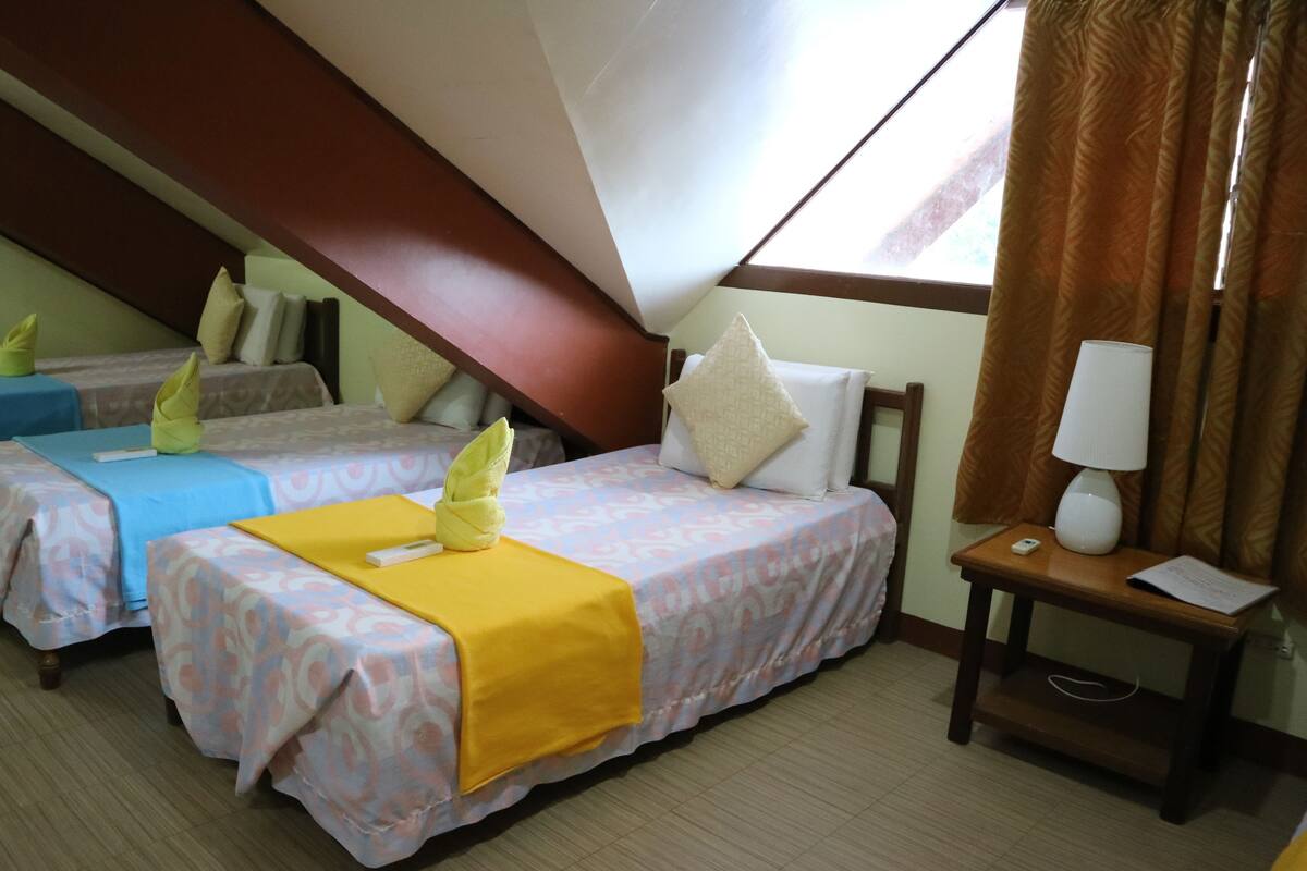 Une chambre d’hôtel avec deux lits, une tête de lit en bois, une table de chevet avec une lampe et une fenêtre avec des rideaux.