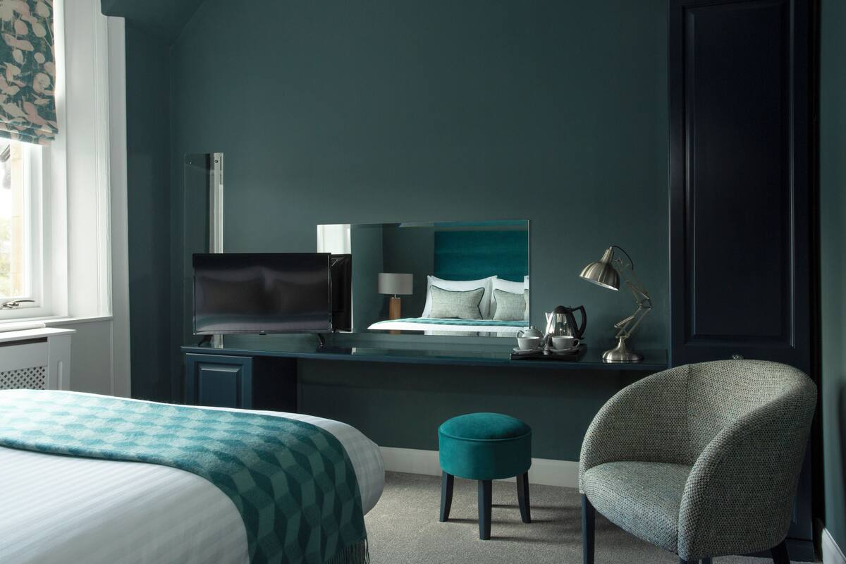 Une chambre d’hôtel moderne dotée d’un grand lit, d’un bureau avec un téléviseur à écran plat, d’un fauteuil confortable et d’un mur d’accent de couleur turquoise.