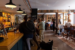 A bar area with wooden shelves stocked with bottles, a counter with a menu, and a dog lying on the floor.
