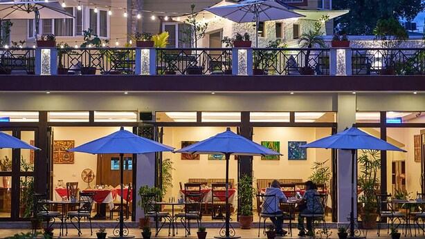 An outdoor dining area with tables and chairs, umbrellas, and potted plants.