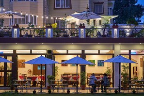Un espacio de comedor al aire libre con mesas, sillas, sombrillas y plantas en macetas.