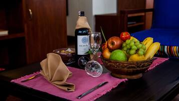 Una mesa con una botella de vino, una copa, un cuenco de fruta y una servilleta sobre un camino de mesa rosa.