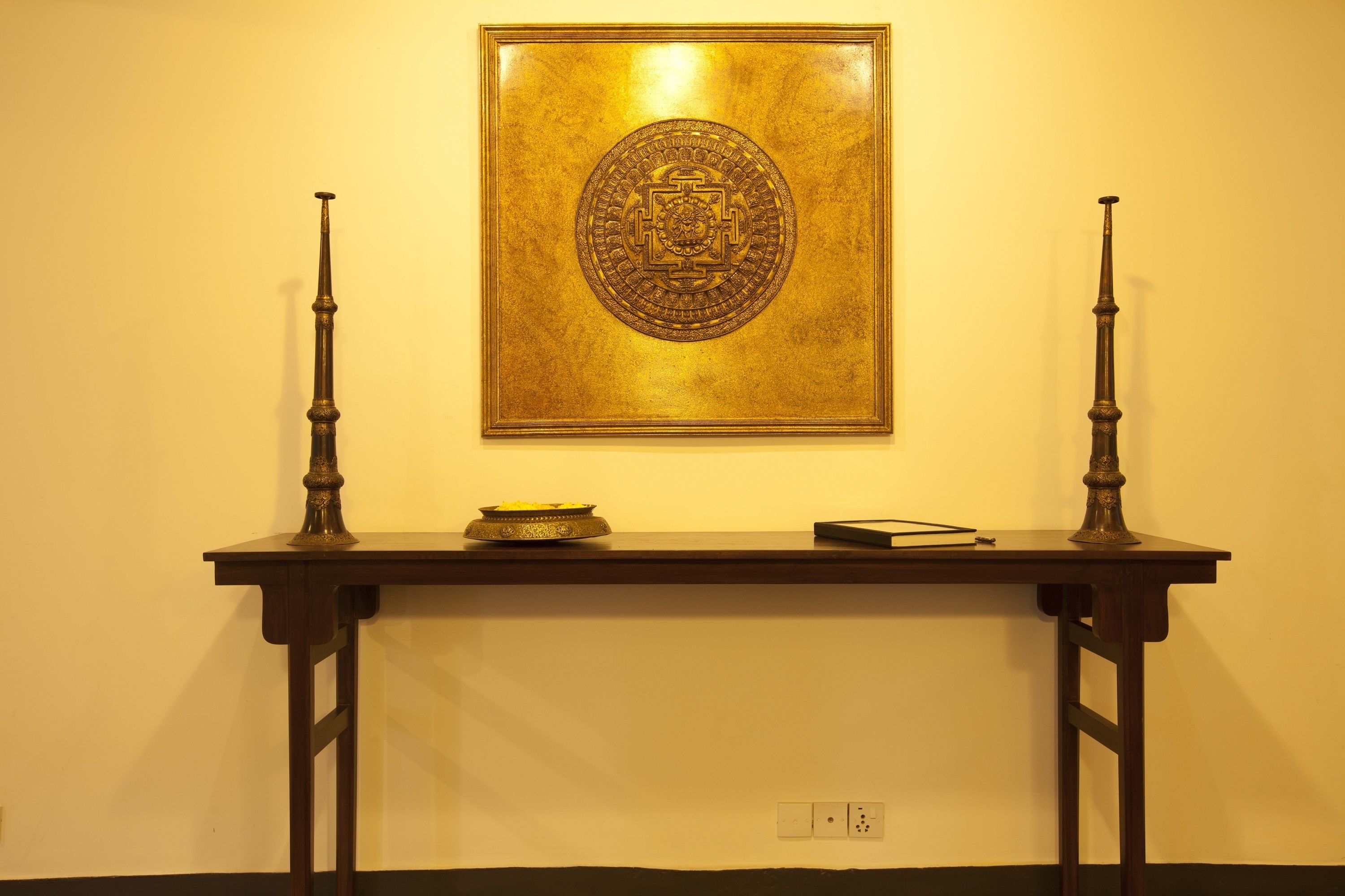 Un emblème encadré est accroché au mur, au-dessus d’une table en bois sur laquelle se trouvent un bol et un livre.