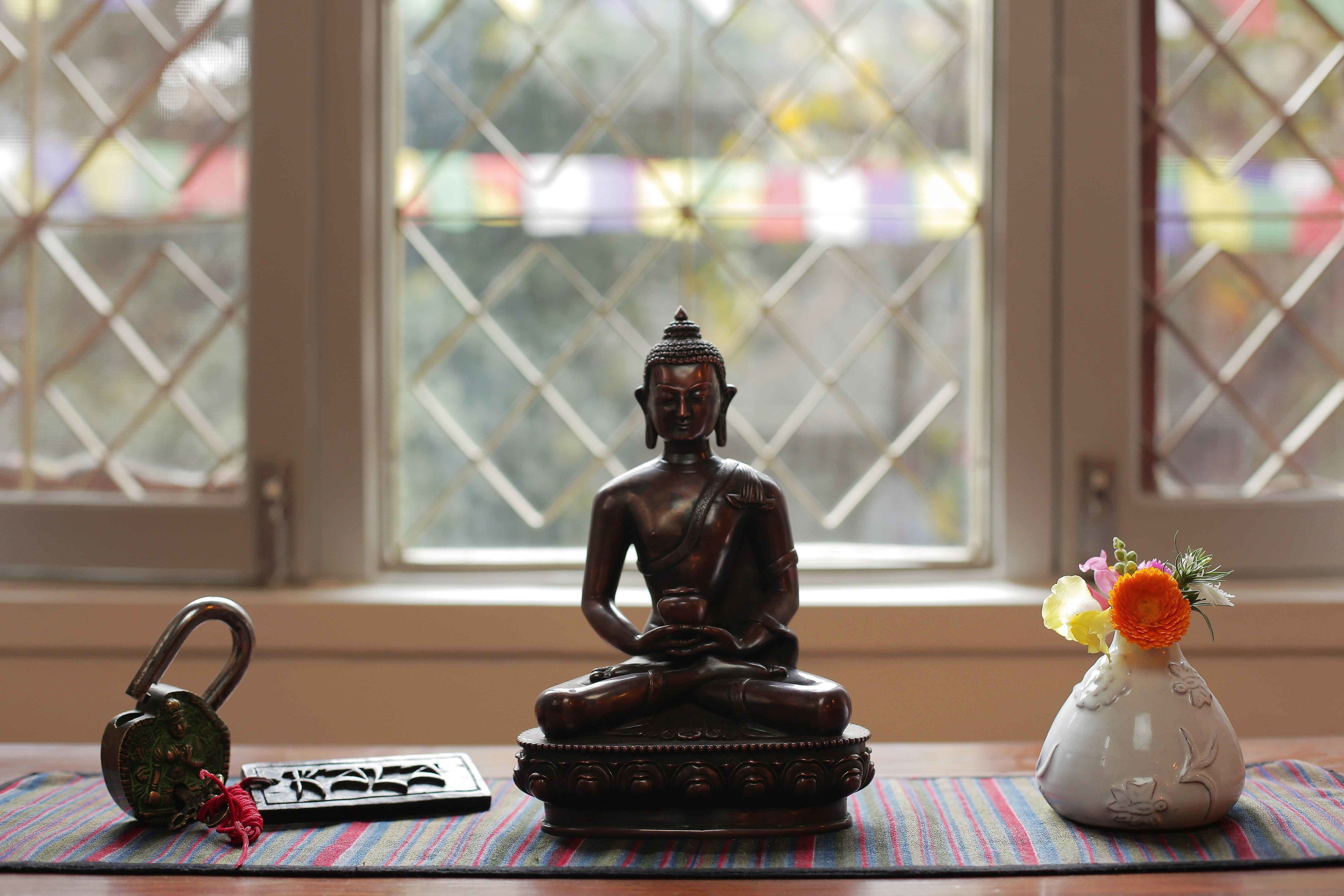 A Buddha statue on a mat, a padlock, and a vase with flowers by a window.