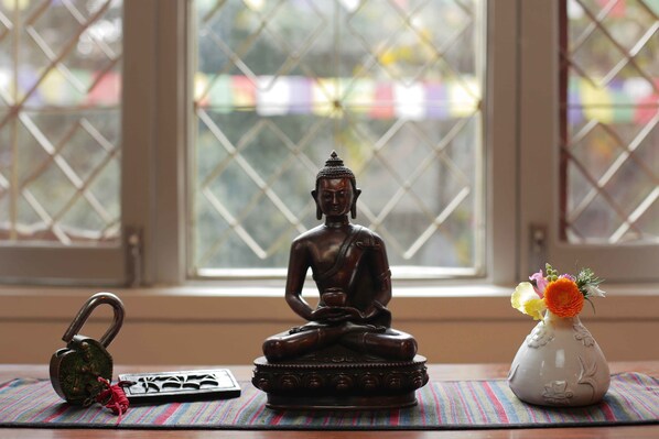 A Buddha statue on a mat, a padlock, and a vase with flowers by a window.