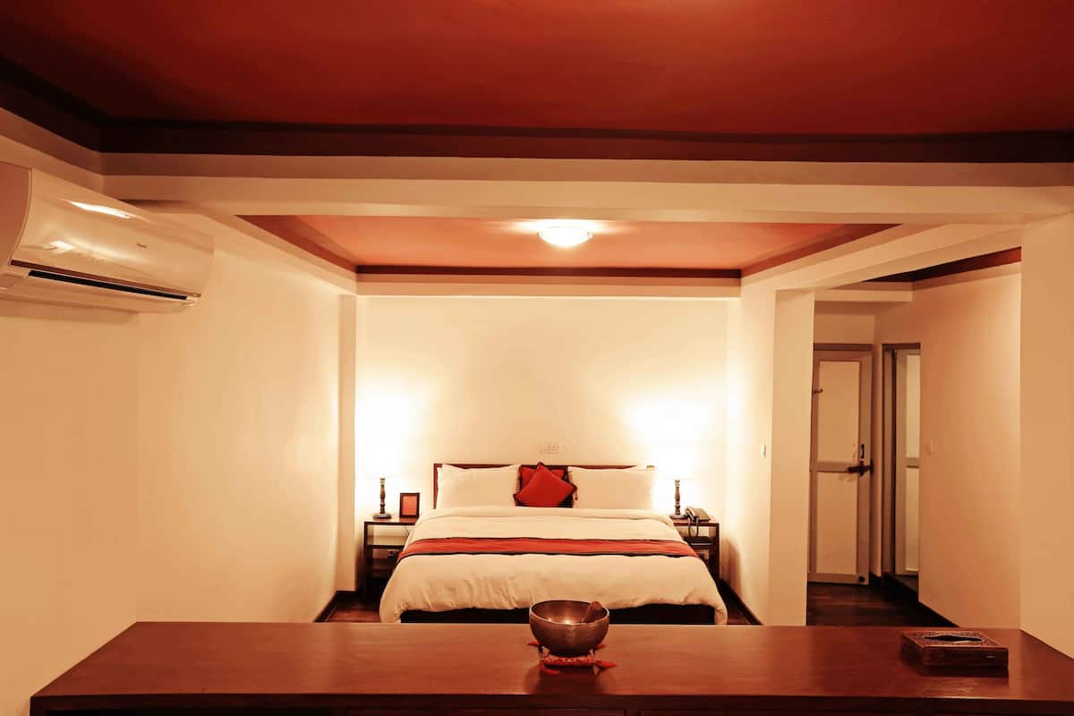 Een hotelkamer met een bed, nachtkastjes, een bijzettafeltje, een tafel met een kom, en een deur die naar een andere kamer leidt.
