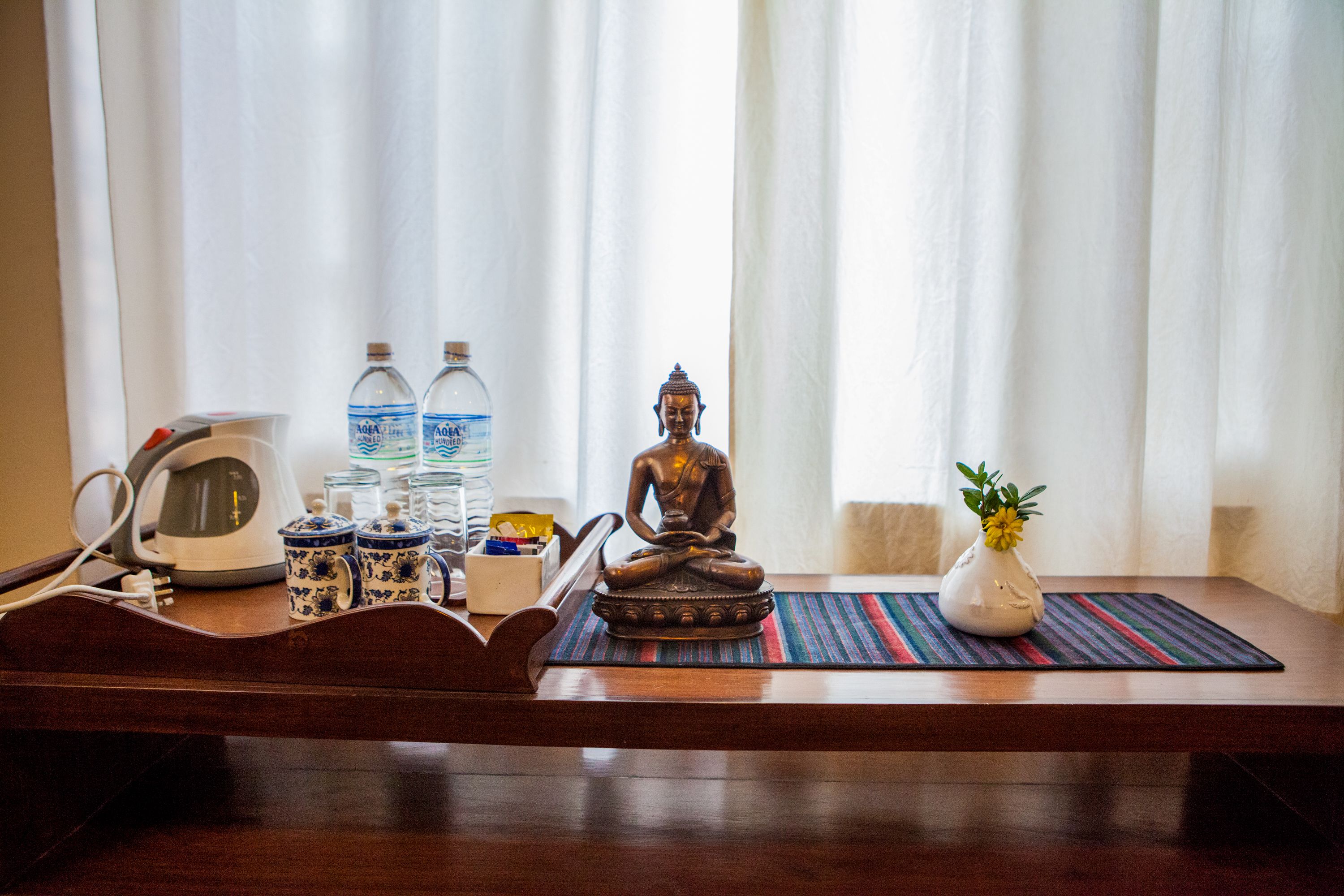 A wooden table with a Buddha statue, a water bottle, a teapot, and a vase with a plant.