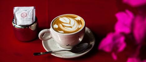 A cup of coffee with latte art on a saucer, a spoon, and a packet of sugar on a red table.