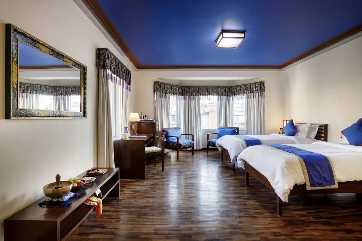 Een hotelkamer met twee bedden, een bureau, een stoel, een spiegel en een houten vloer.