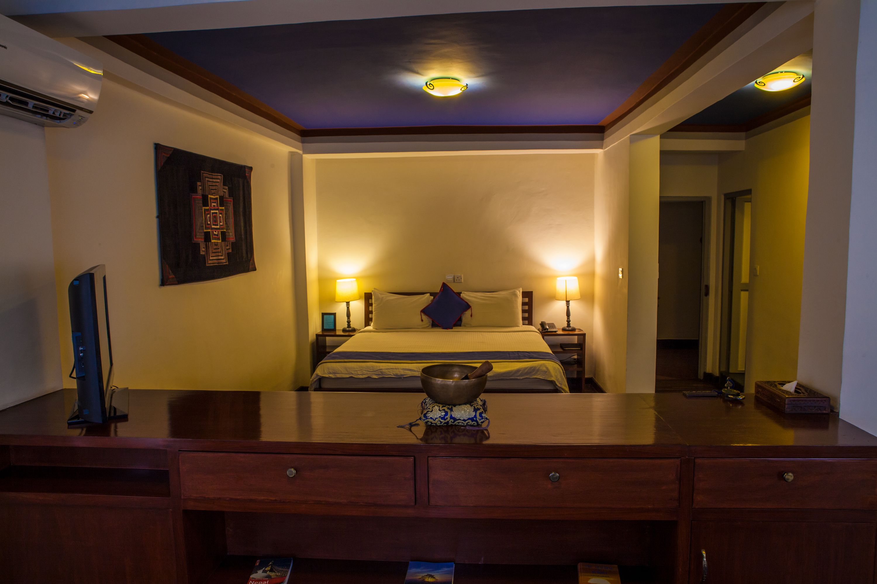 Une chambre d’hôtel avec un lit, des lampes de chevet, un bureau avec un bol et un tableau encadré au mur.