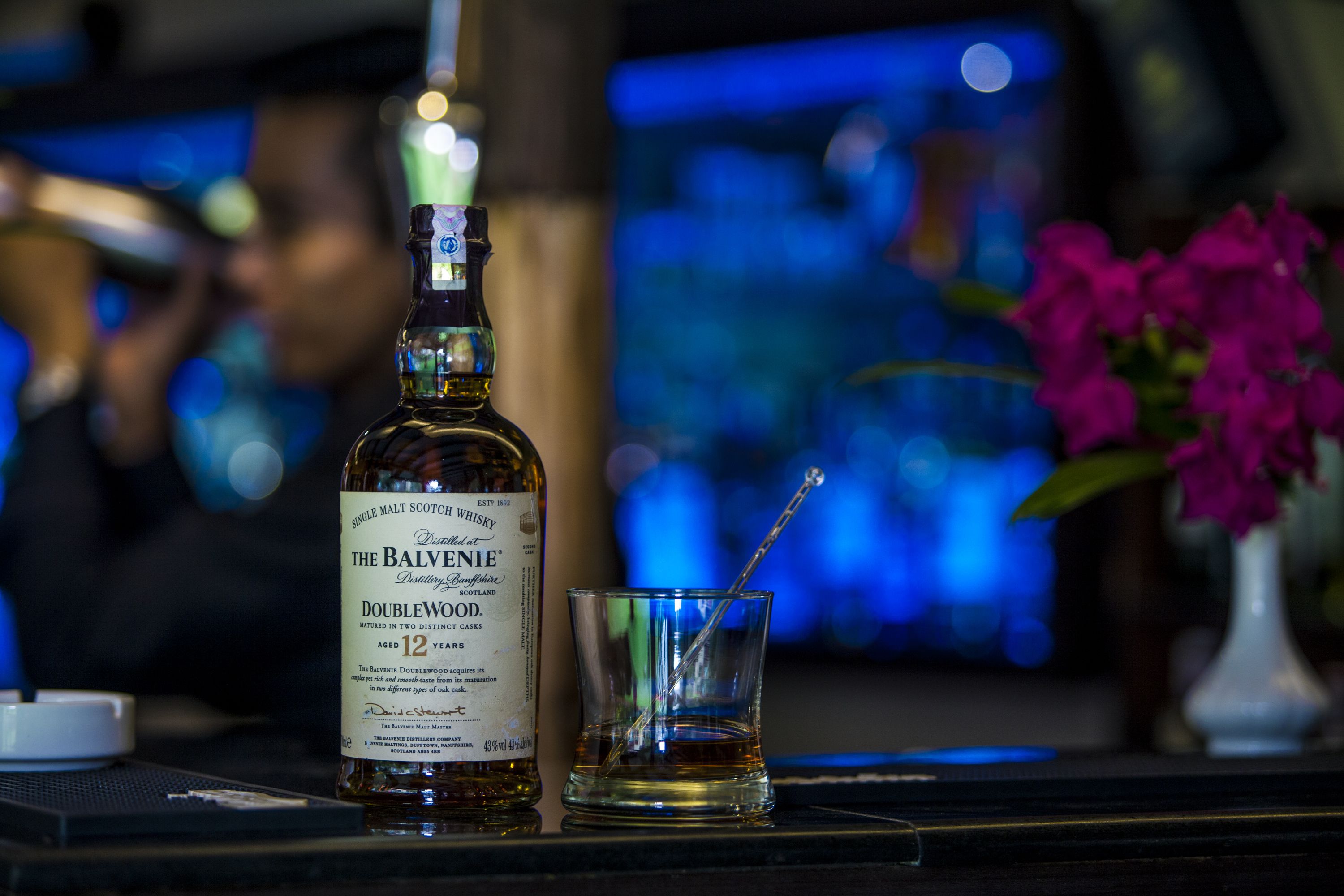Eine Flasche The Balvenie DoubleWood Whisky und ein Glas mit Trinkhalm auf einer Bar.