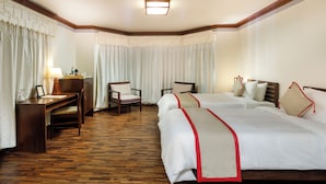 A hotel room with two beds, a desk, a chair, and a lamp.