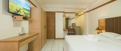 A hotel room with a bed, a desk, a television mounted on the wall, and a ceiling fan.