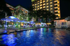 A swimming pool with people in it, surrounded by outdoor seating areas and palm trees. - Orchid Inn Resort (Angeles City)