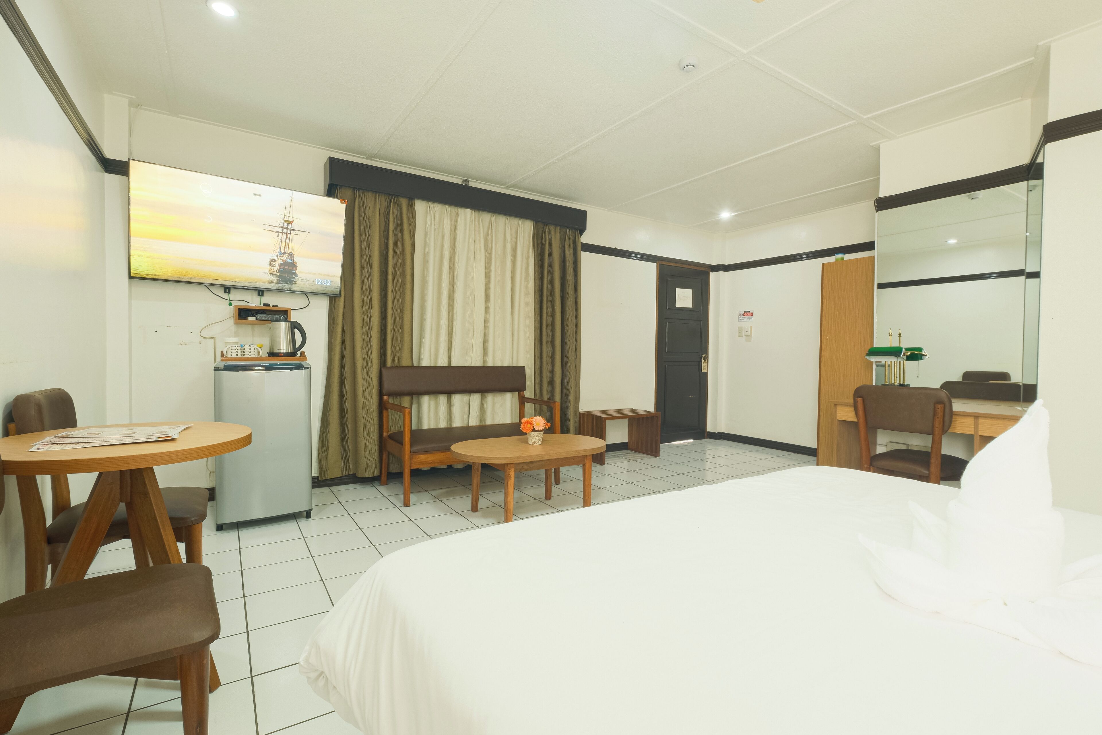 Una habitación de hotel con cama, escritorio, silla, mesita y kitchenette.