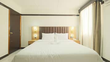 Una camera d'albergo con un letto grande, due comodini, una testiera con illuminazione integrata, una porta e una finestra con tende.