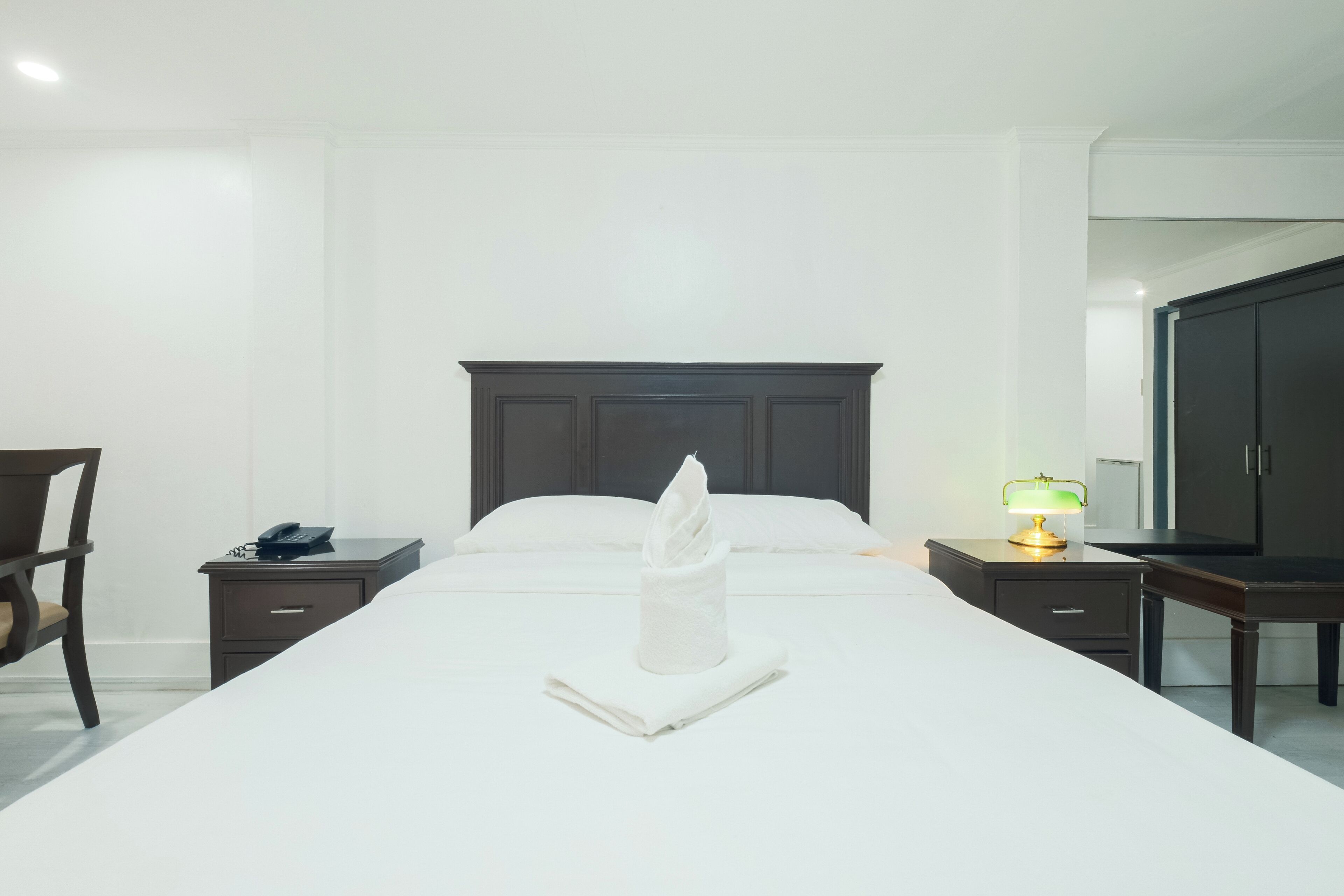 A hotel room with a neatly made bed, a bedside table with a lamp, a chair, and a wardrobe.