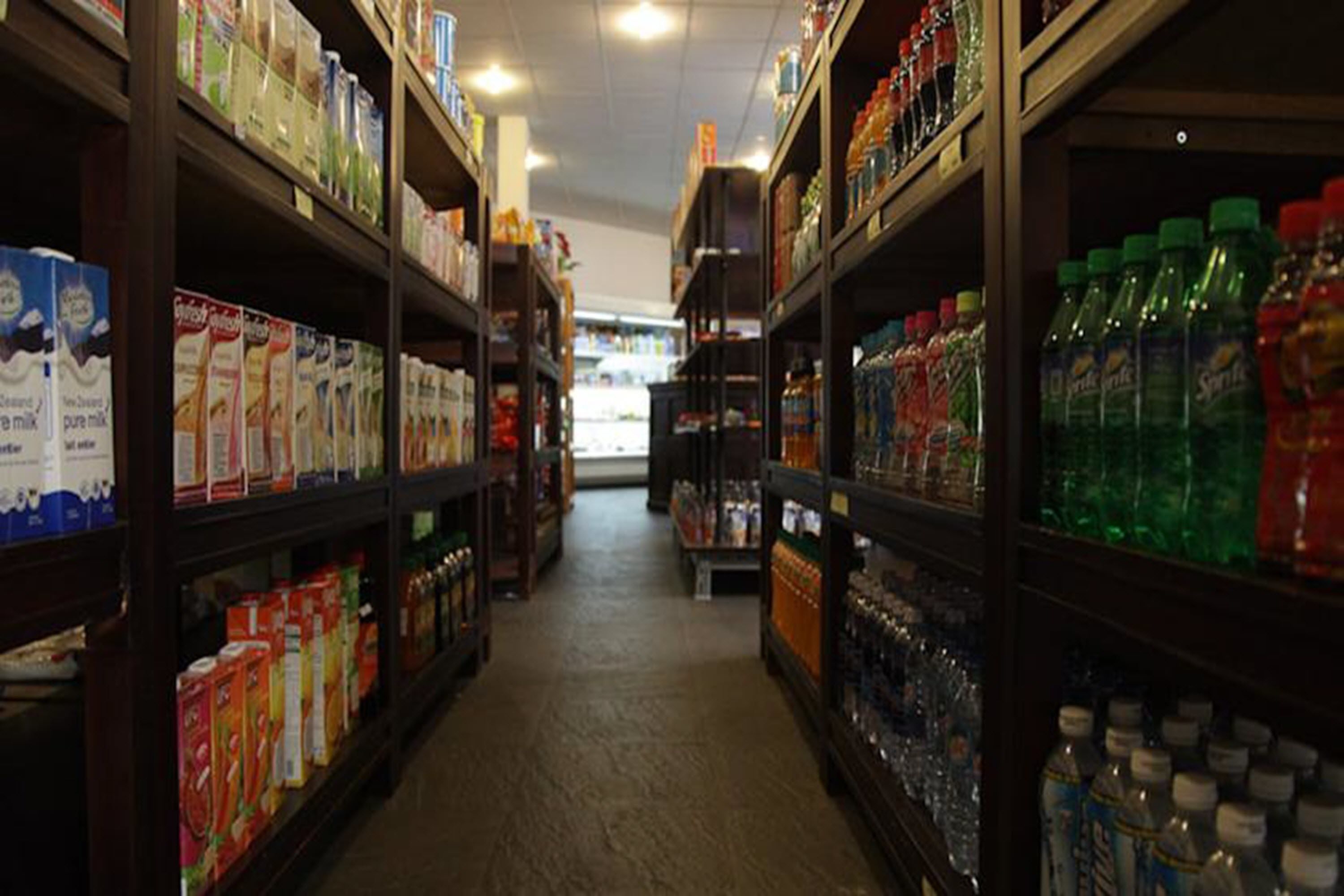 Een gang in een supermarkt met schappen vol verschillende producten, waaronder melk, ontbijtgranen en flessenwater.