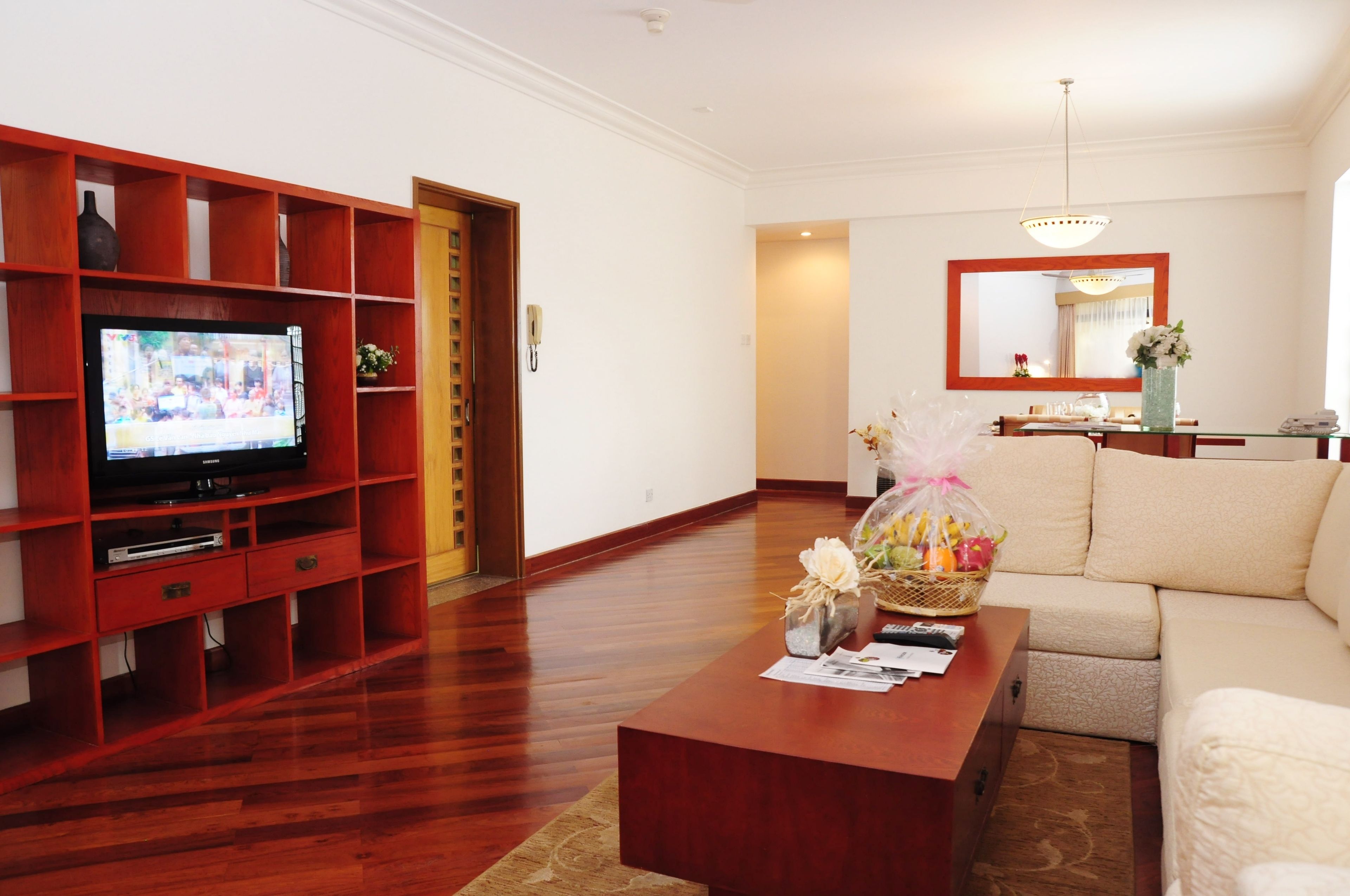 Een woonkamer met een houten tv-meubel, een televisie, een bank en een salontafel met een mand vol bloemen.