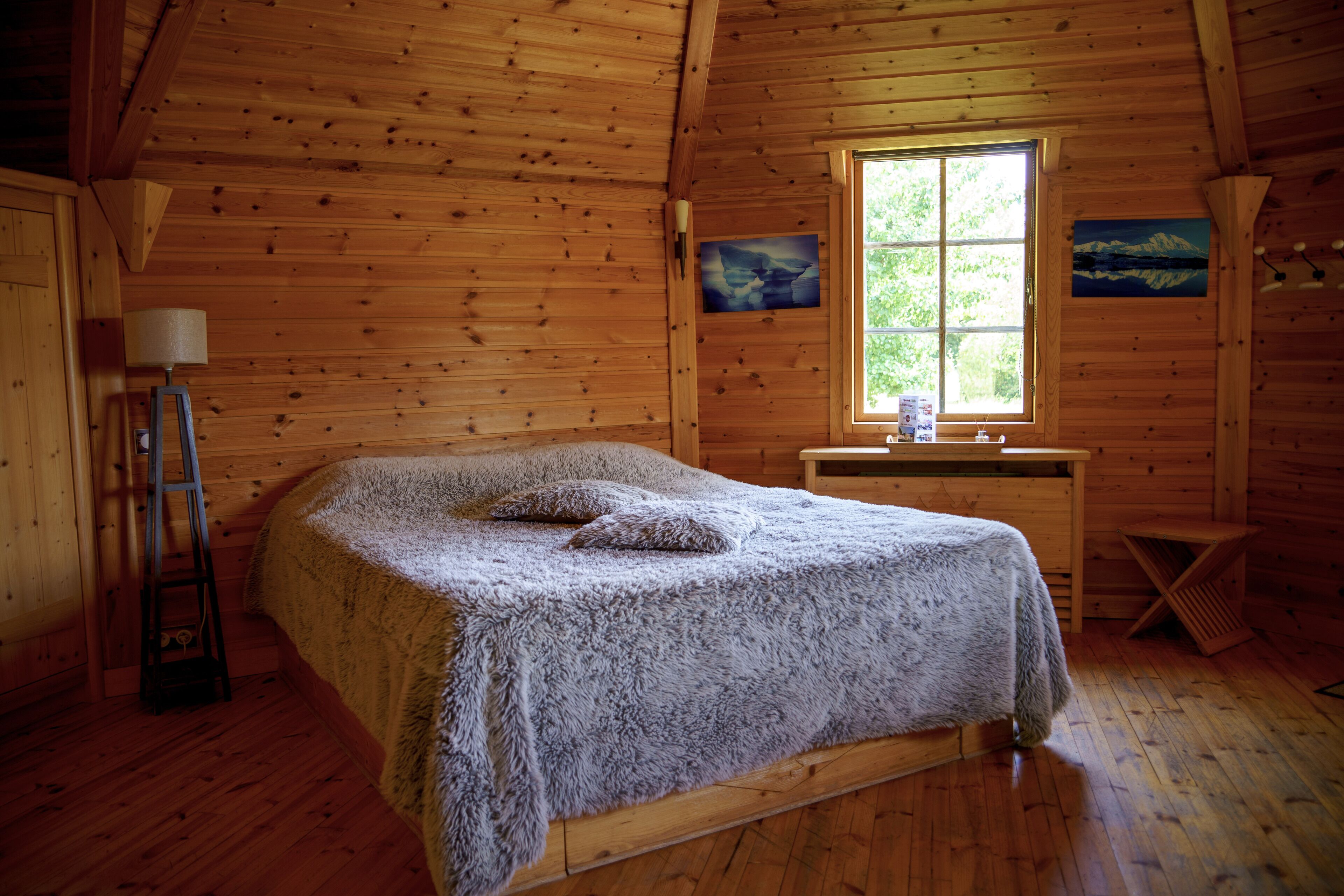 Un dormitorio de cabaña de madera con una cama, una ventana y un cuadro en la pared.