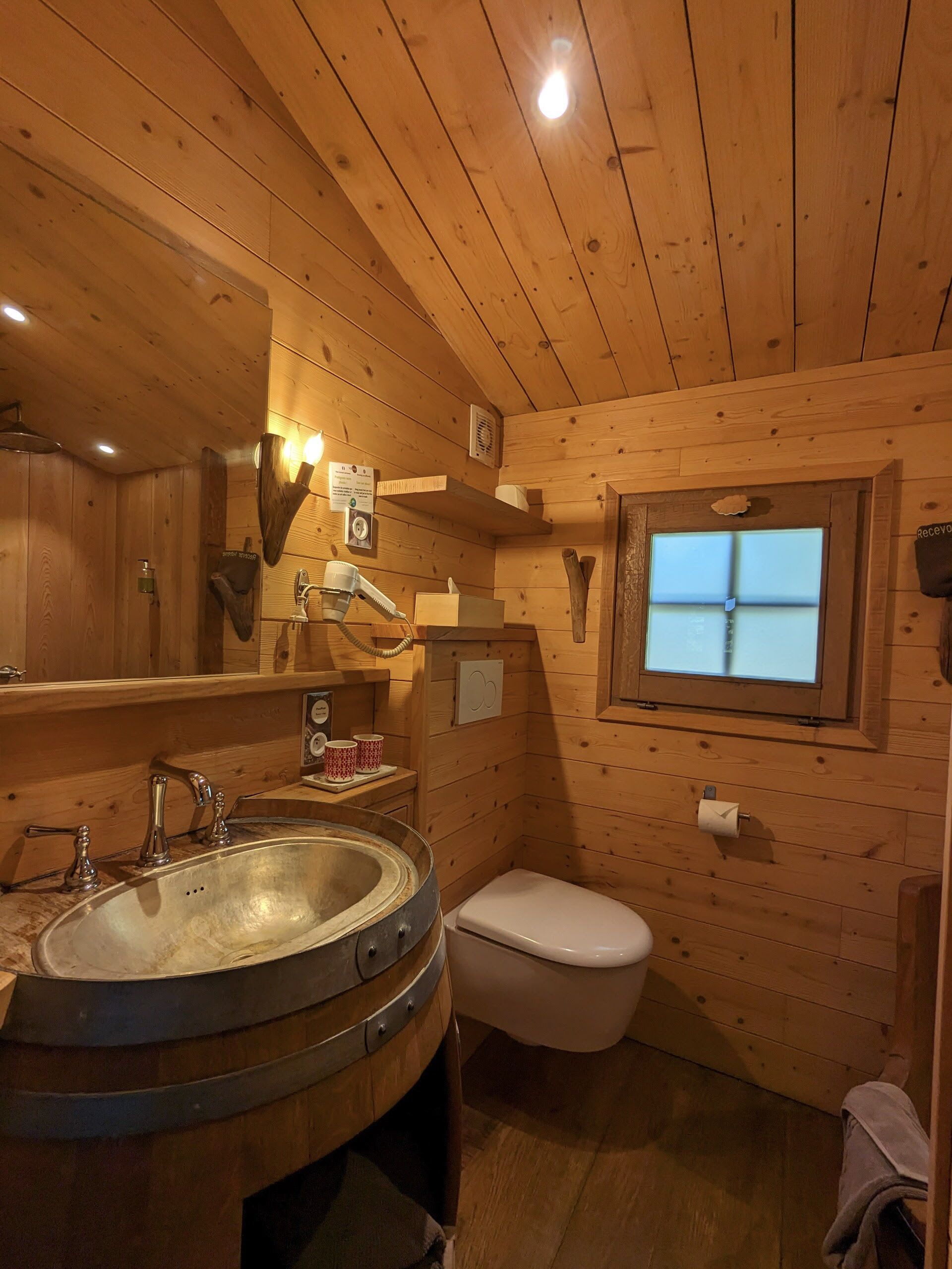 Ein Badezimmer in einer Holzhütte mit Waschbecken, Toilette und einem Fenster.