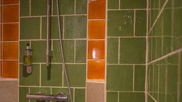 Un área de ducha con azulejos verdes y anaranjados, un cabezal de ducha de mano y un dispensador de jabón.