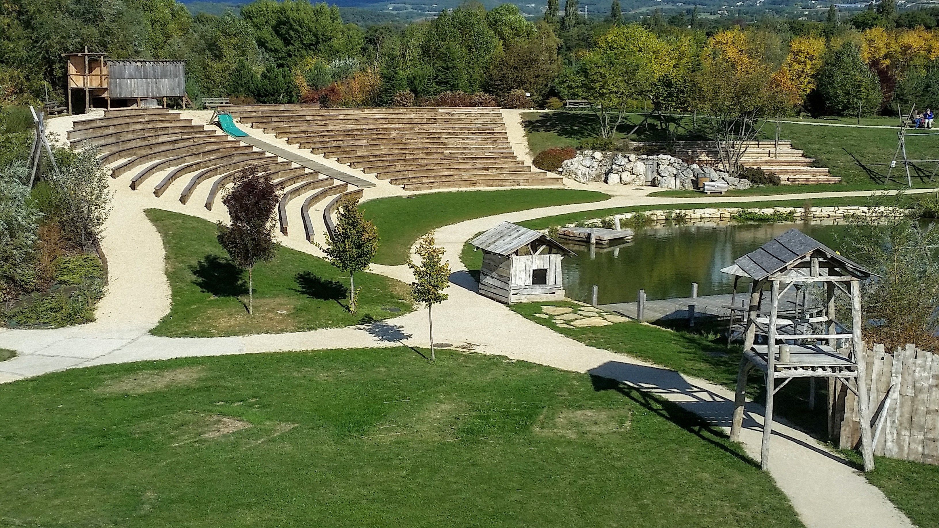 Un anfiteatro al aire libre con asientos escalonados, un pequeño estanque y una estructura de madera.