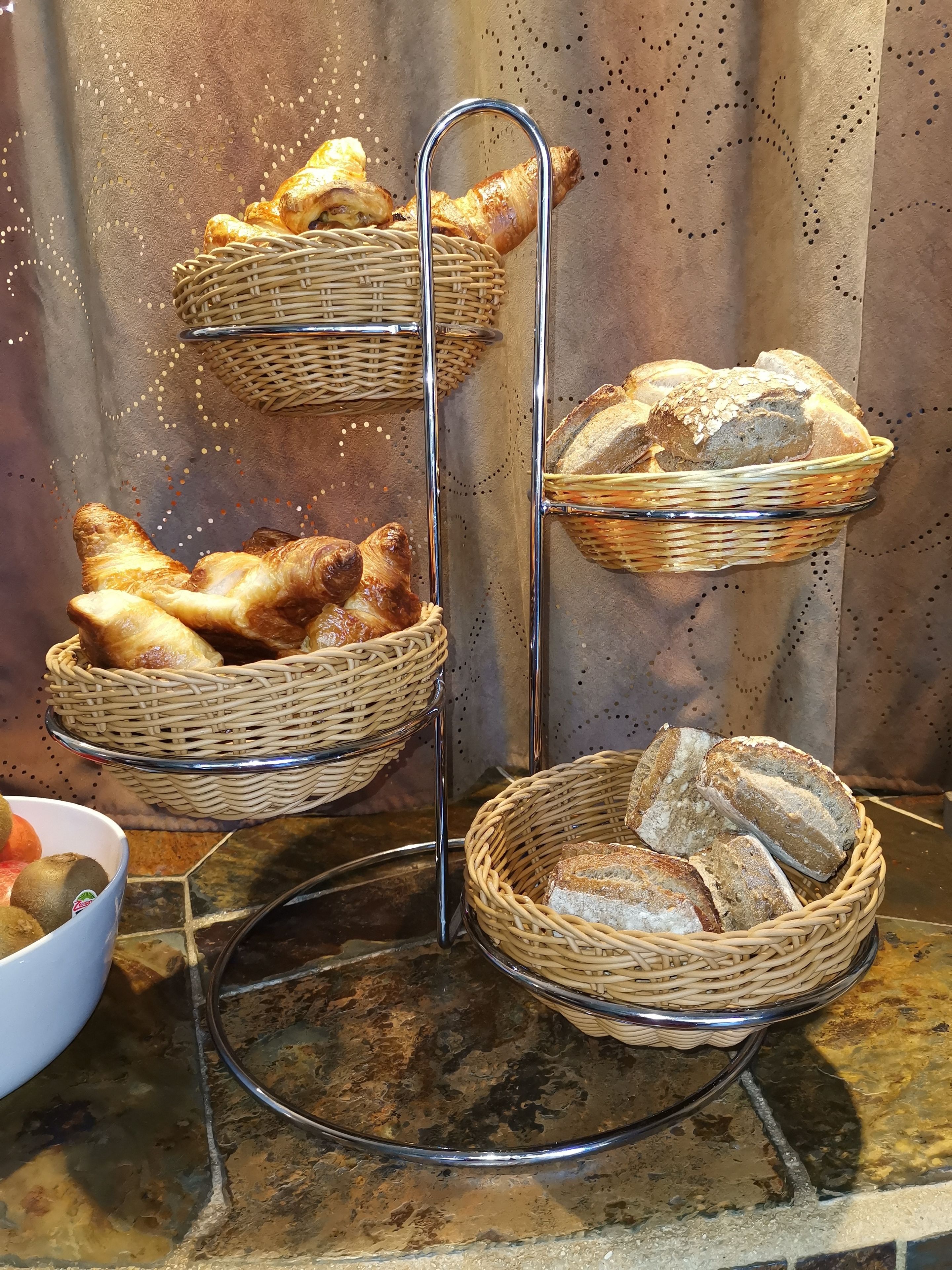 A display of bread and pastries in wicker baskets on a metal stand.