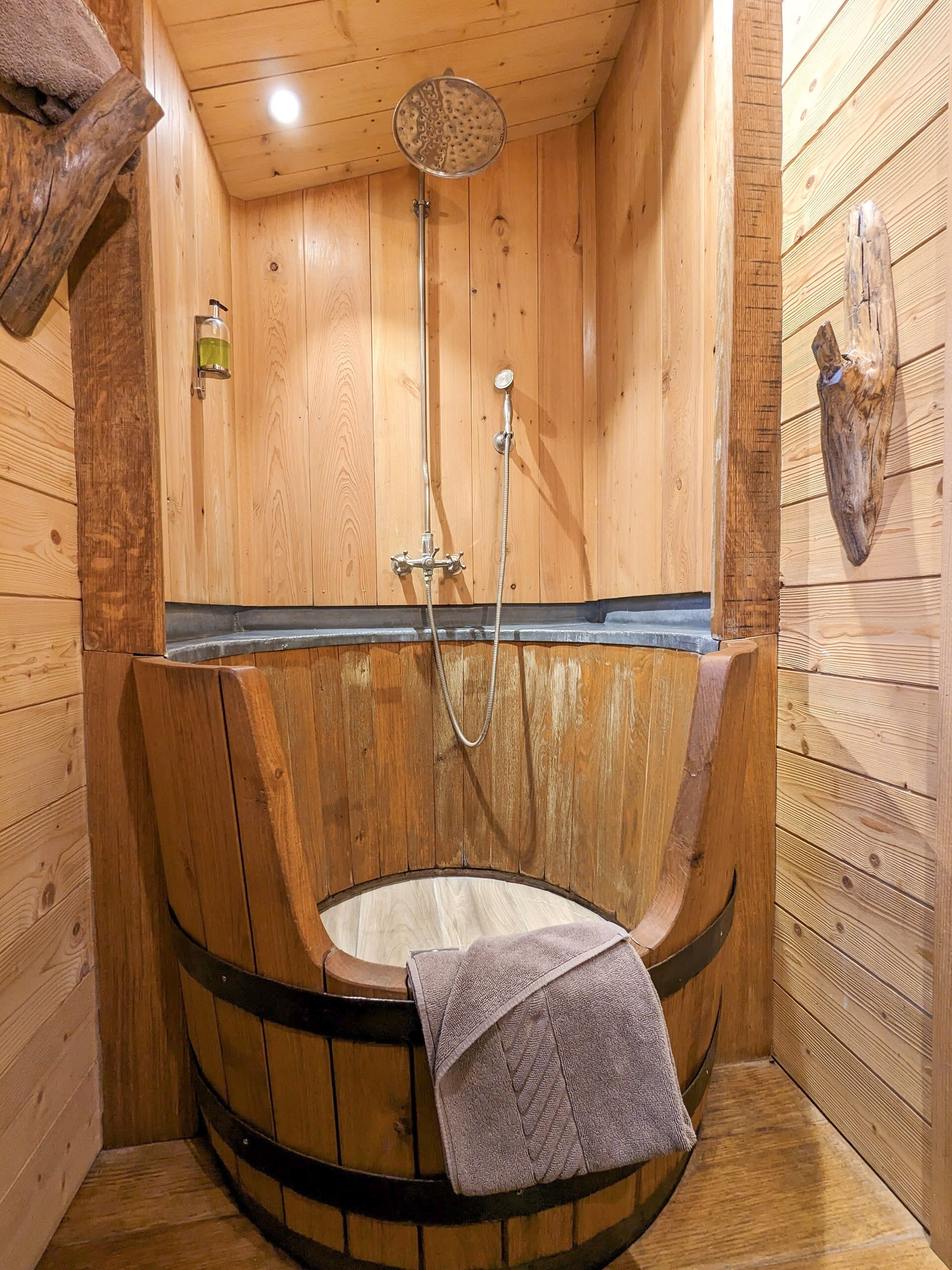 Eine Holzsauna mit einer Holzwanne, einer Duschbrause und einem Handtuch, das über der Wanne hängt.