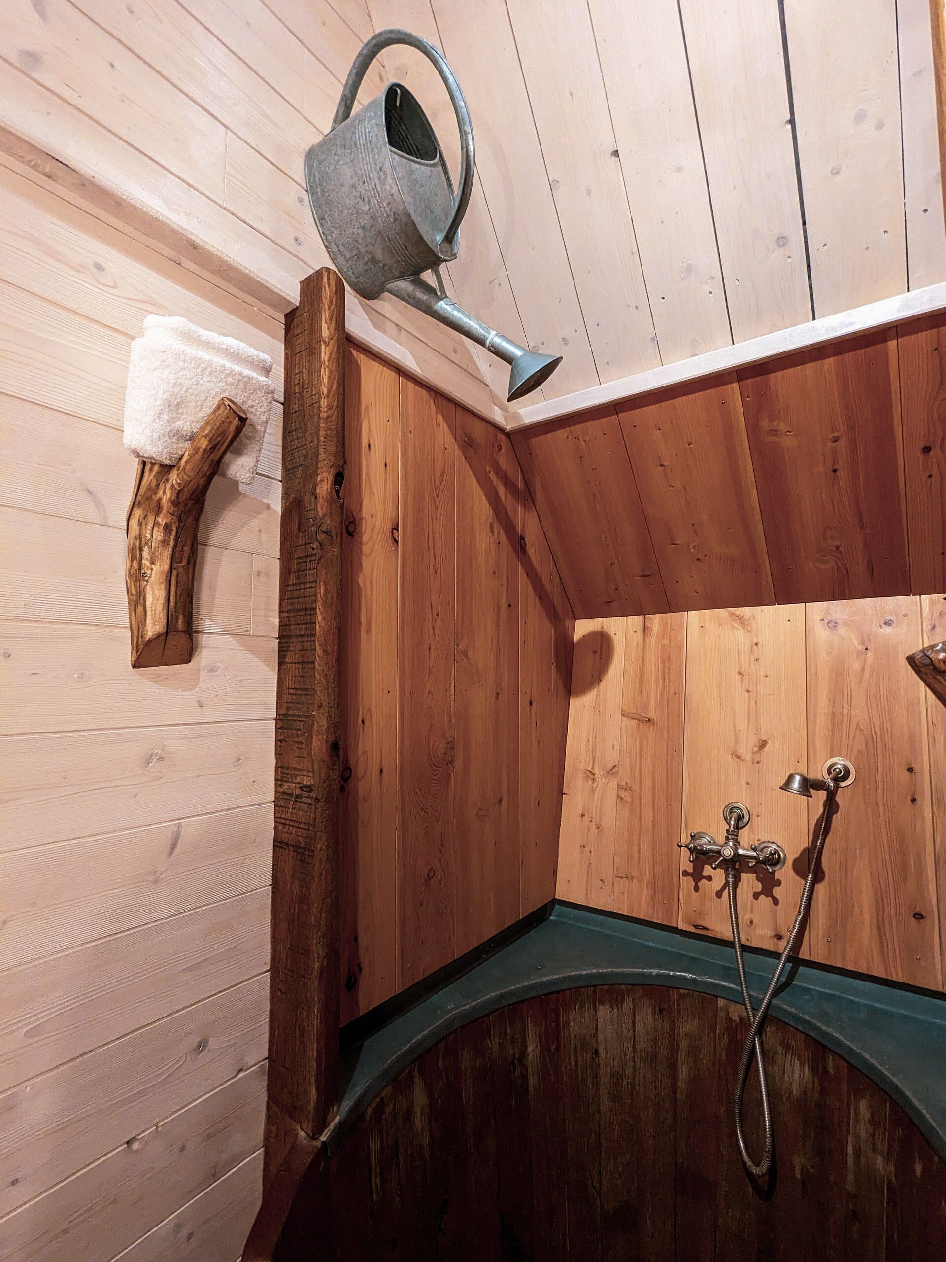 A wooden sauna with a wooden bench, a metal showerhead, and a metal watering can.