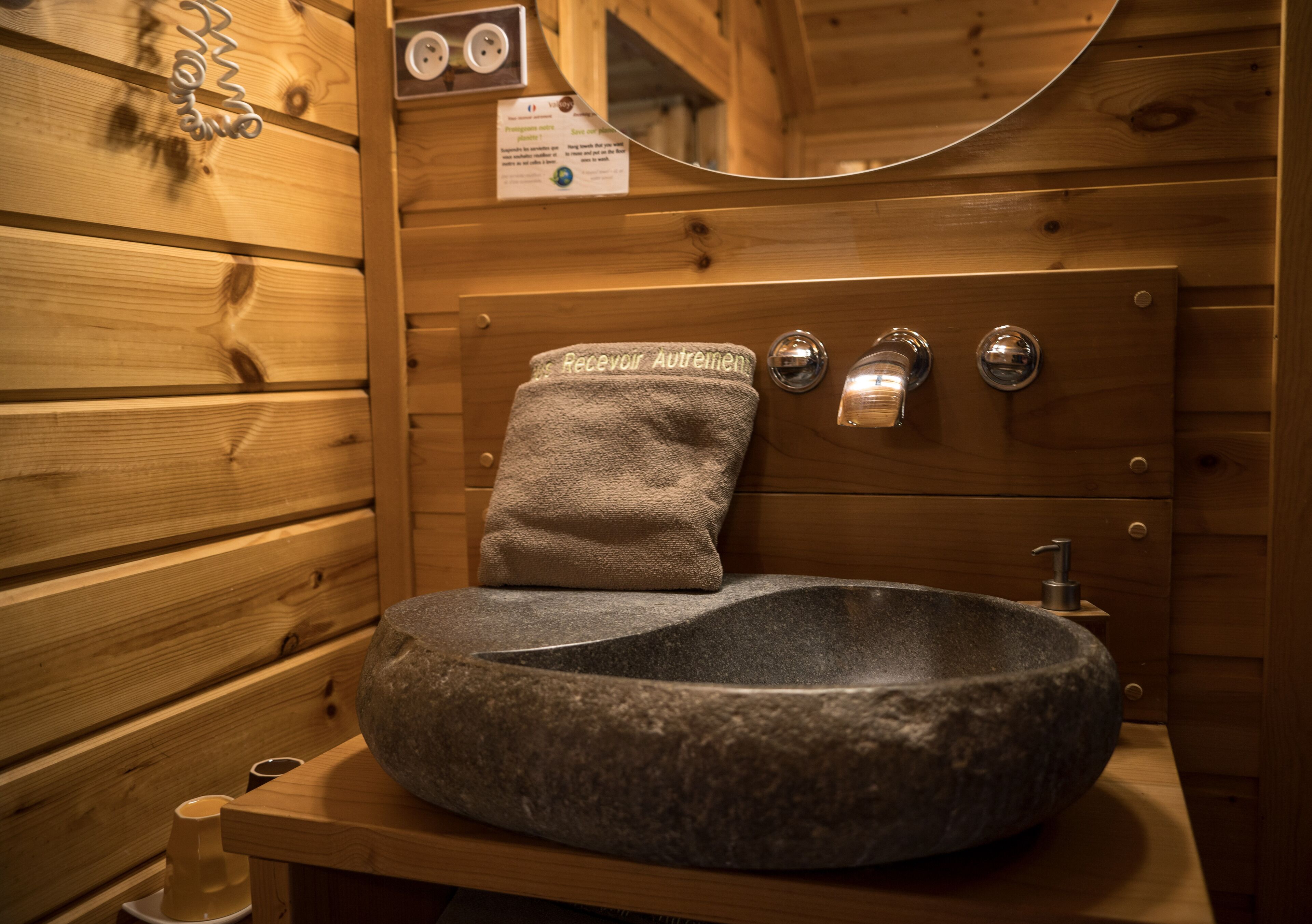 Ein Steinkopfwaschbecken in einem Badezimmer einer Holzjagdhaus, mit einem Handtuch an der Wand und einem Spiegel darüber.