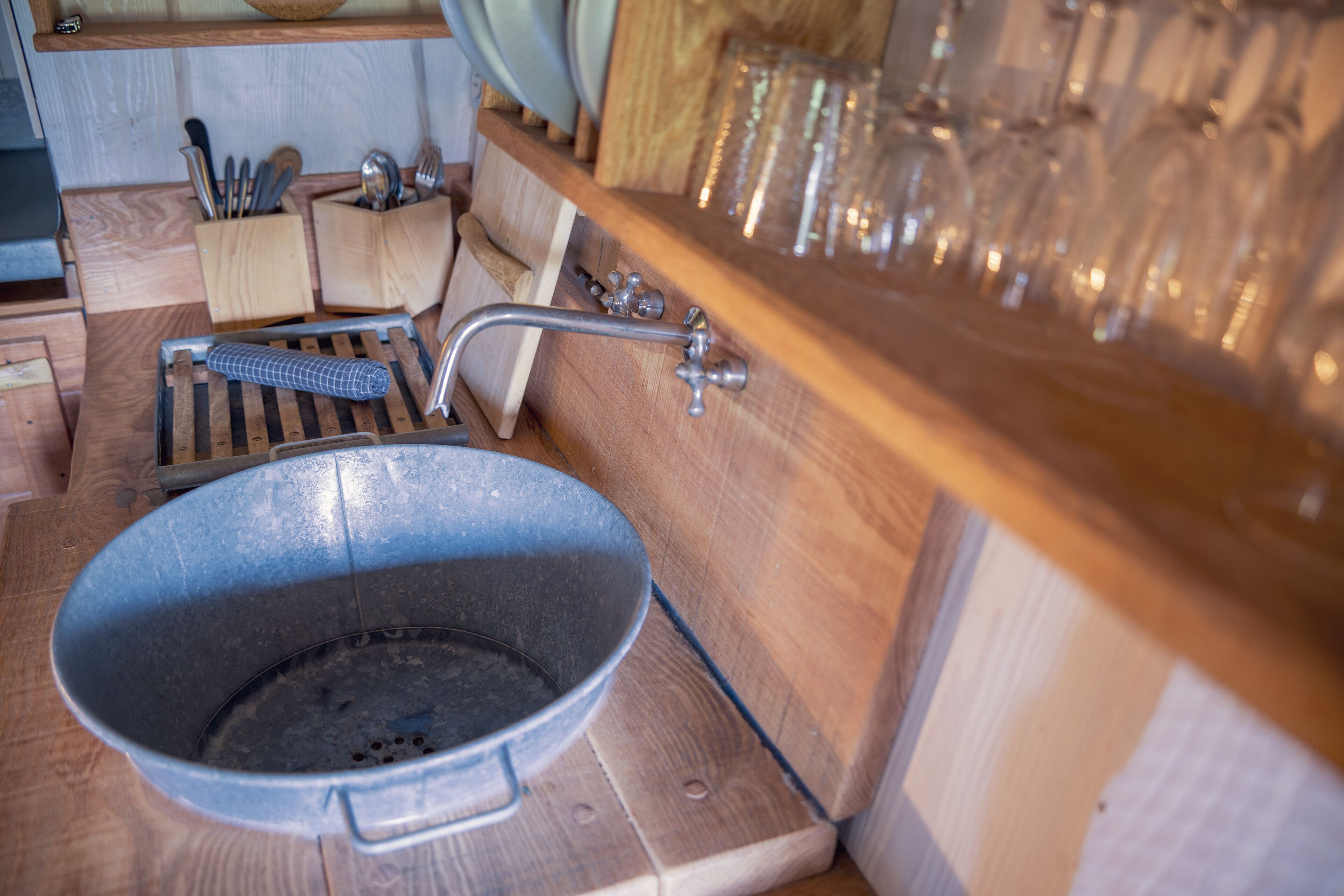 A rustic kitchen with a large metal pan, wooden utensils, and a glassware rack.