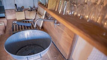 A rustic kitchen with a large metal pan, wooden utensils, and a glassware rack.