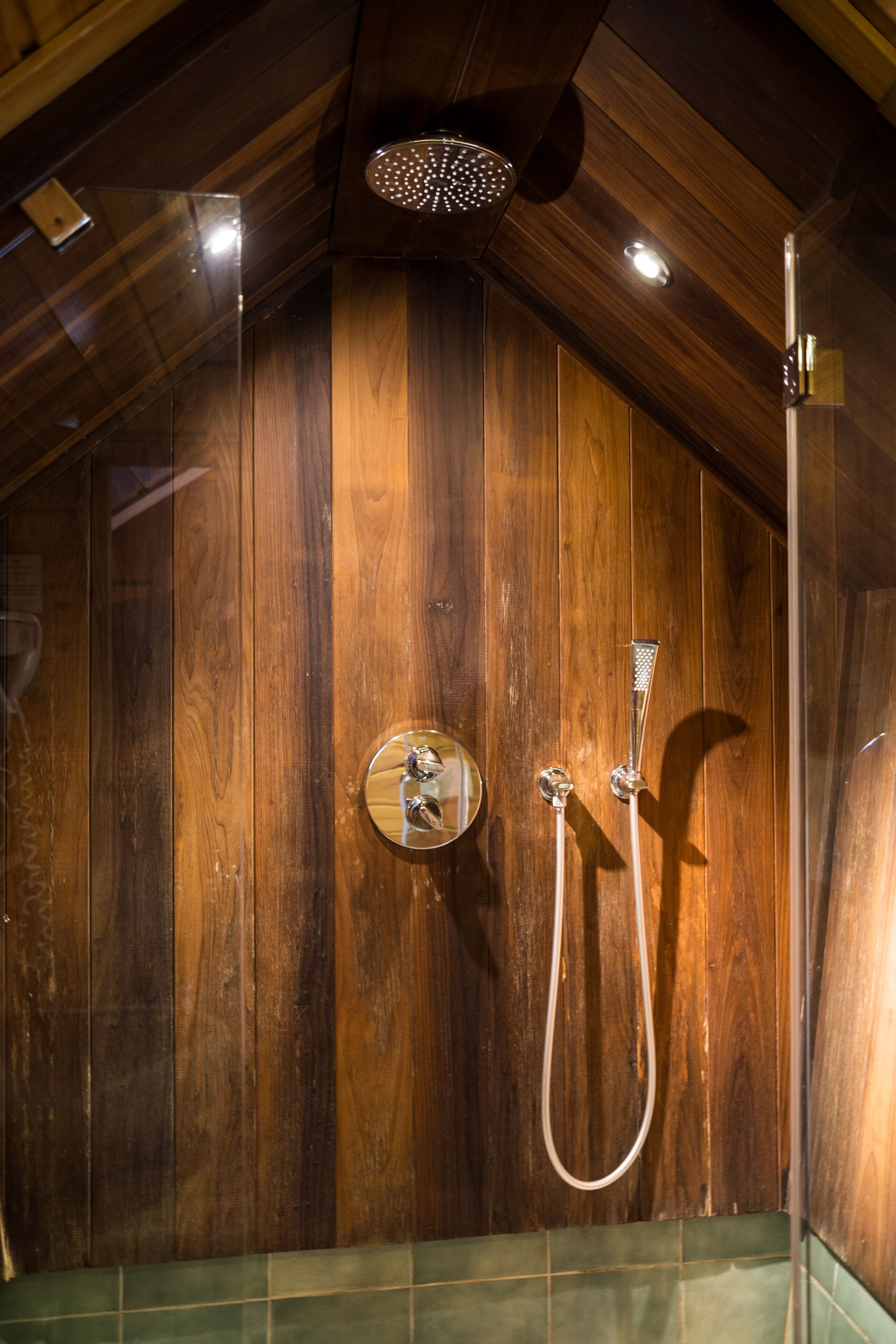 A wooden shower enclosure with a handheld showerhead and a wall-mounted faucet.